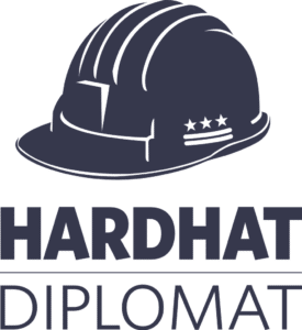 The Logo of HardHat Diplomat. The front of a hardhat, with the Washington, DC coat of arms of three stars over two bars on the side of the hardhat. The hardhat floats over the business name.